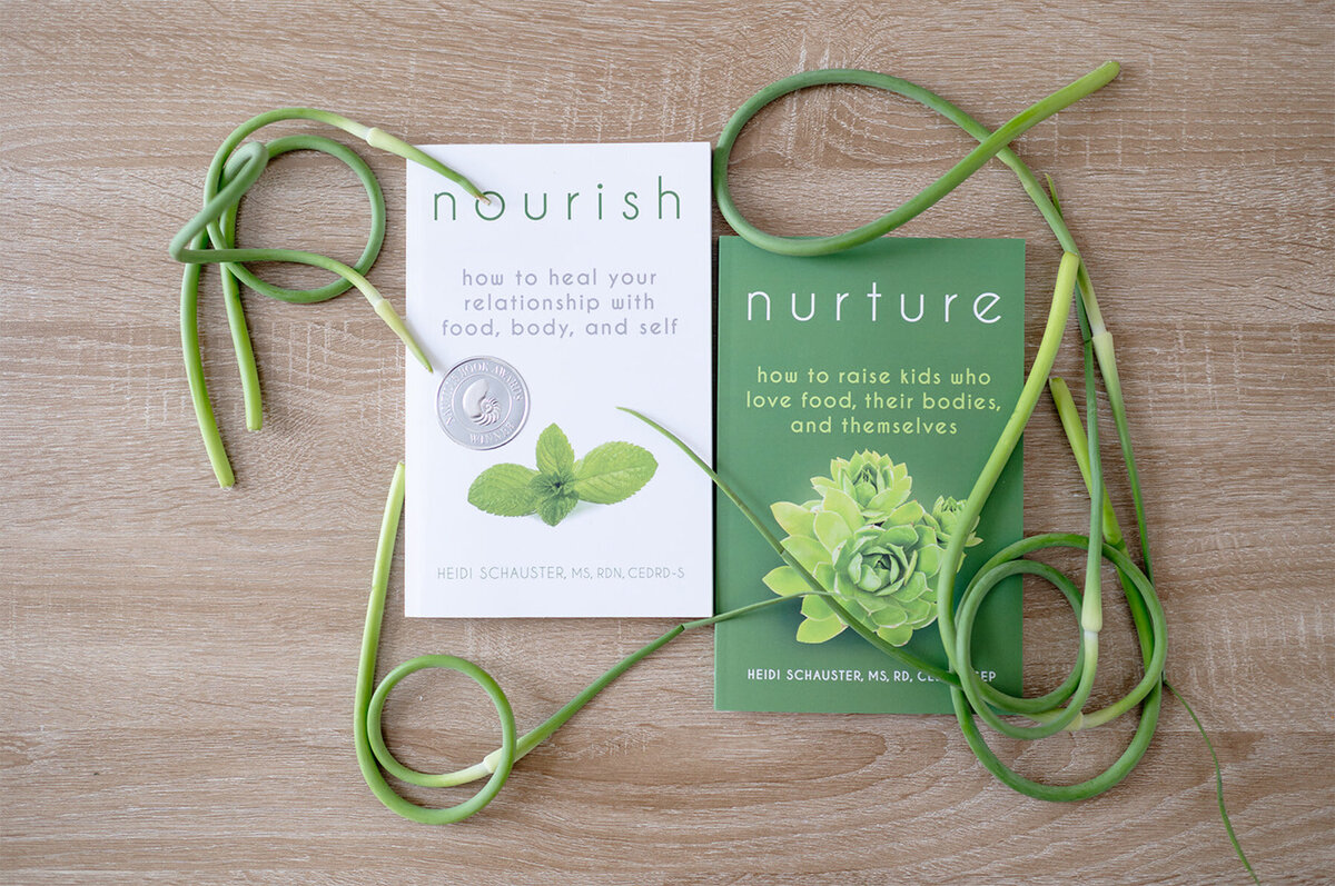 Two books by Heidi Schauster on healing relationships with food, adorned with a green leaf and a green ribbon.
