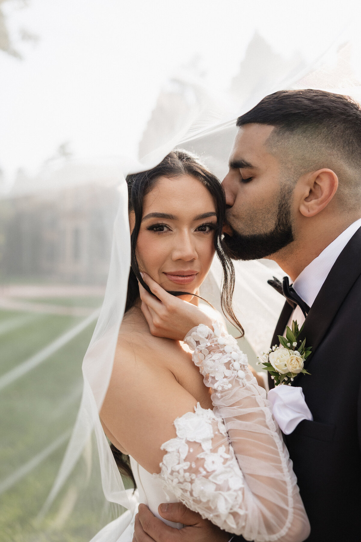 Bride looking into the camera as her groom kisses her on the cheek.