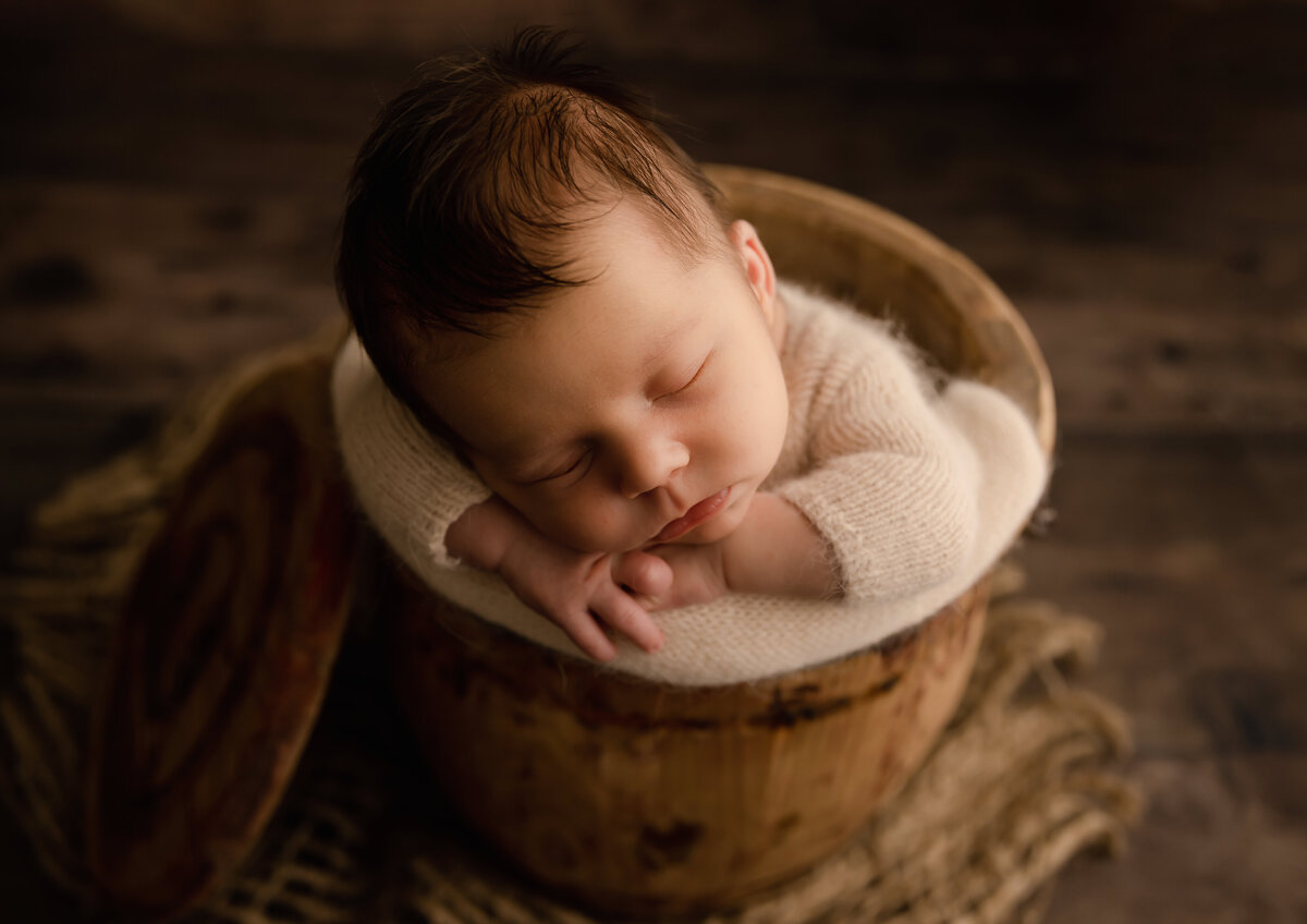 baby boy in bucket wearing a white cute outfit on wood backgrounf near dupont