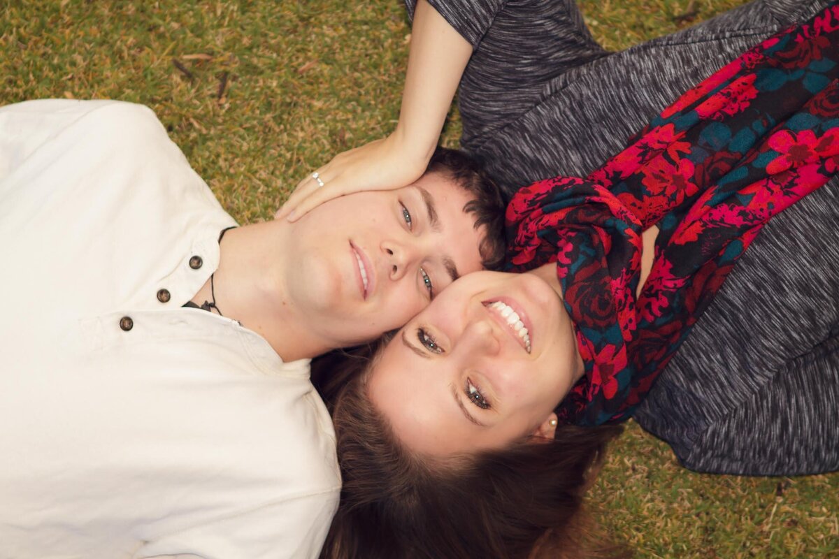 Engagement portrait looking down at a couple lying on their backs with their heads together.