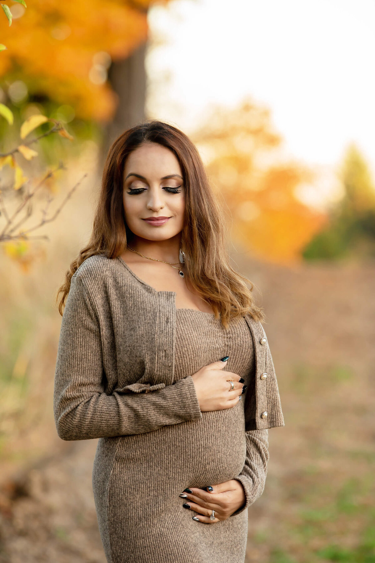 mom to be cradling her belly in a Toronto field in the fall.