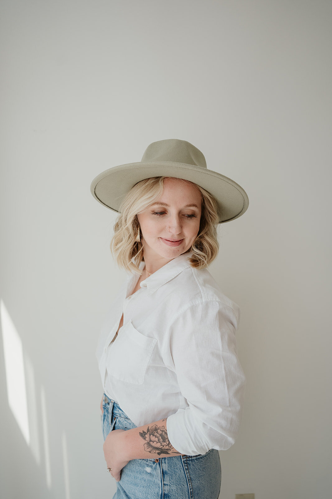 Side portrait of a woman in a hat standing in soft window light during a Kalamazoo Michigan Wildher and Co branding session.