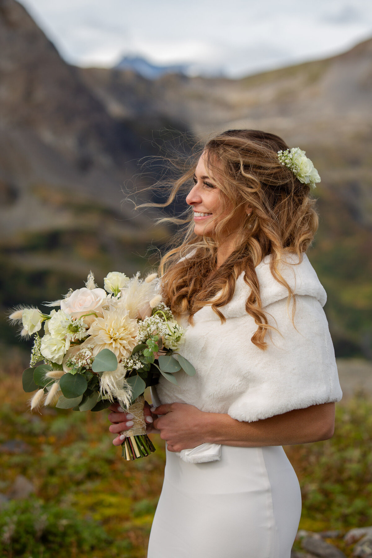 A bride stands smiling with her wedding bouquet on her elopement day.