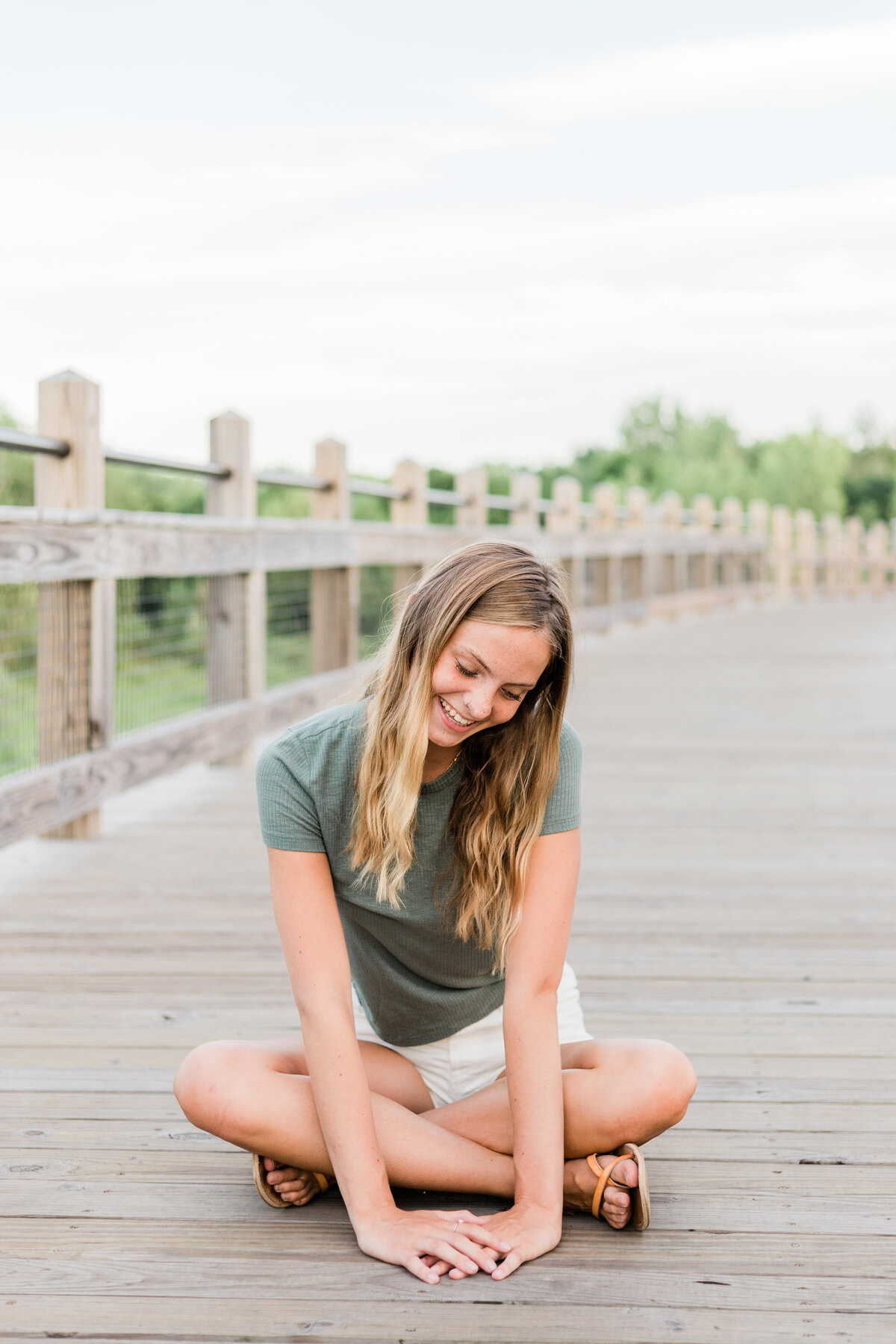 girl sitting cross legged on a bridge looking and smiling at the ground