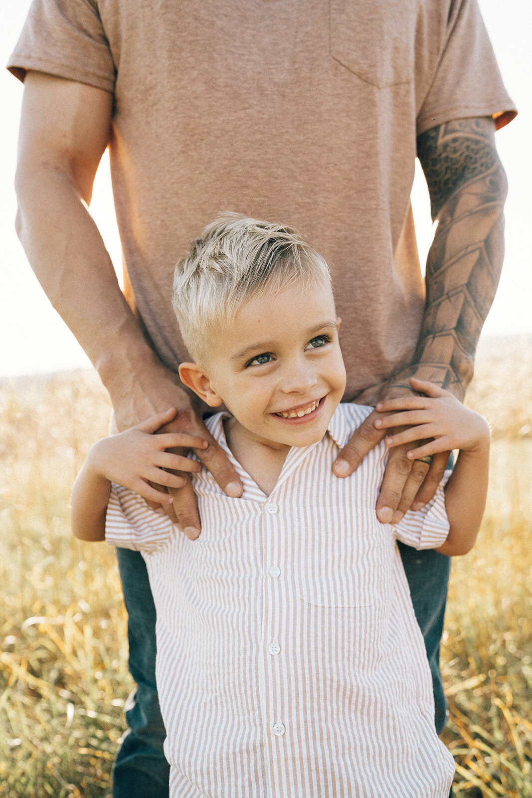 Dad gently holding his son’s shoulders as they stand in a field during a candid family session