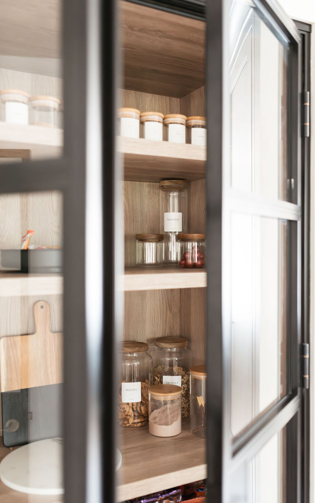 Built-in pantry cabinet with glass doors with black frames. Inside the open doors are spices organized in glass jars.