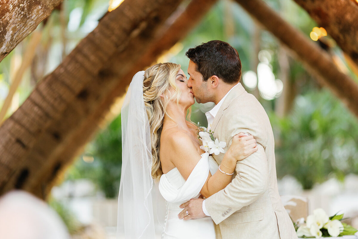 Monica and Austyn share a romantic first kiss under a rustic wooden arch at their tropical Islamorada wedding.