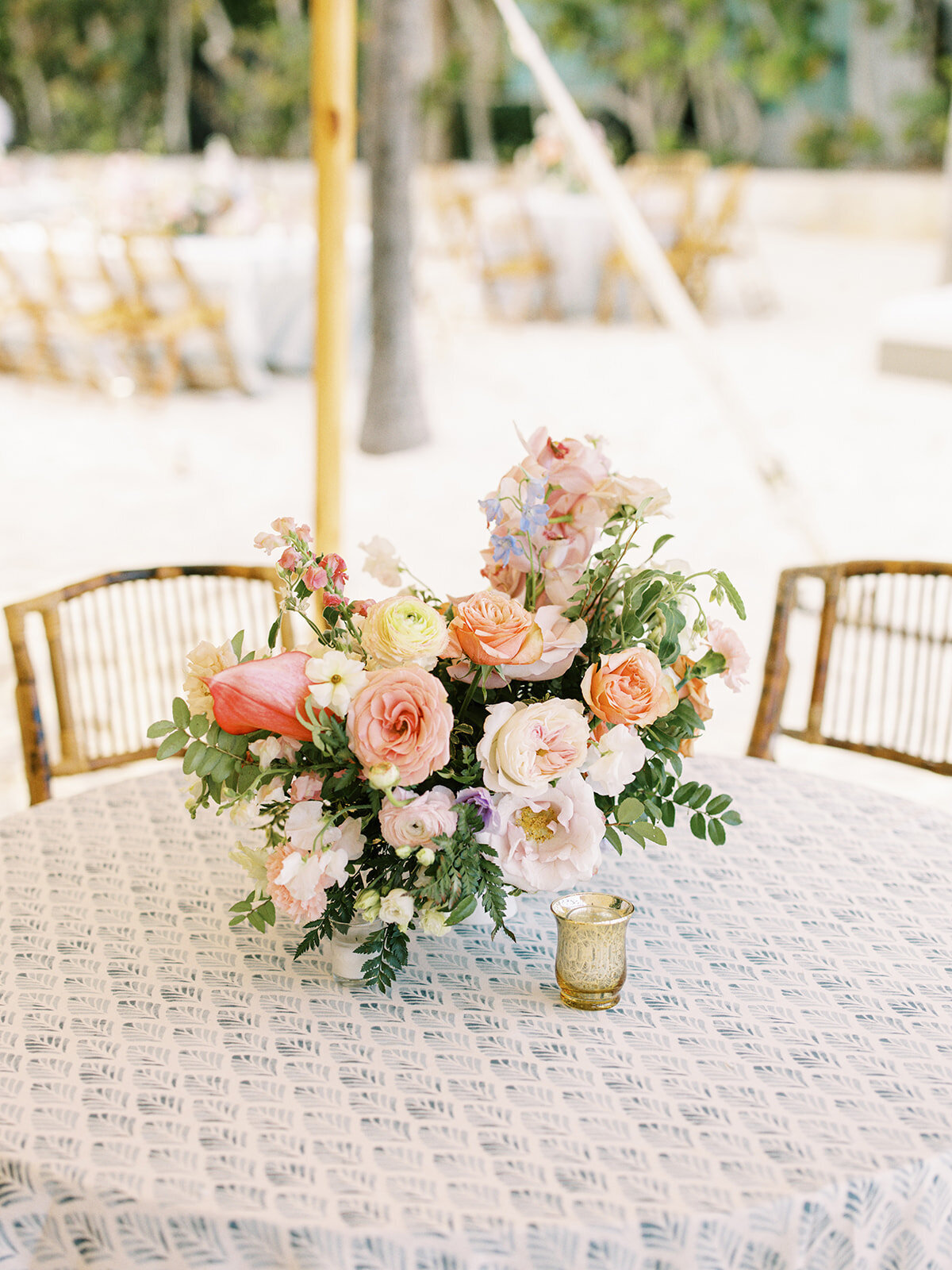 Lush low floral centerpieces for small tables at tropical destination wedding reception. Private estate tented beach wedding in Exuma, Bahamas. Pink, orange, dusty blue, lavender, and natural green flowers. Destination floral design by Rosemary & Finch Floral Design.
