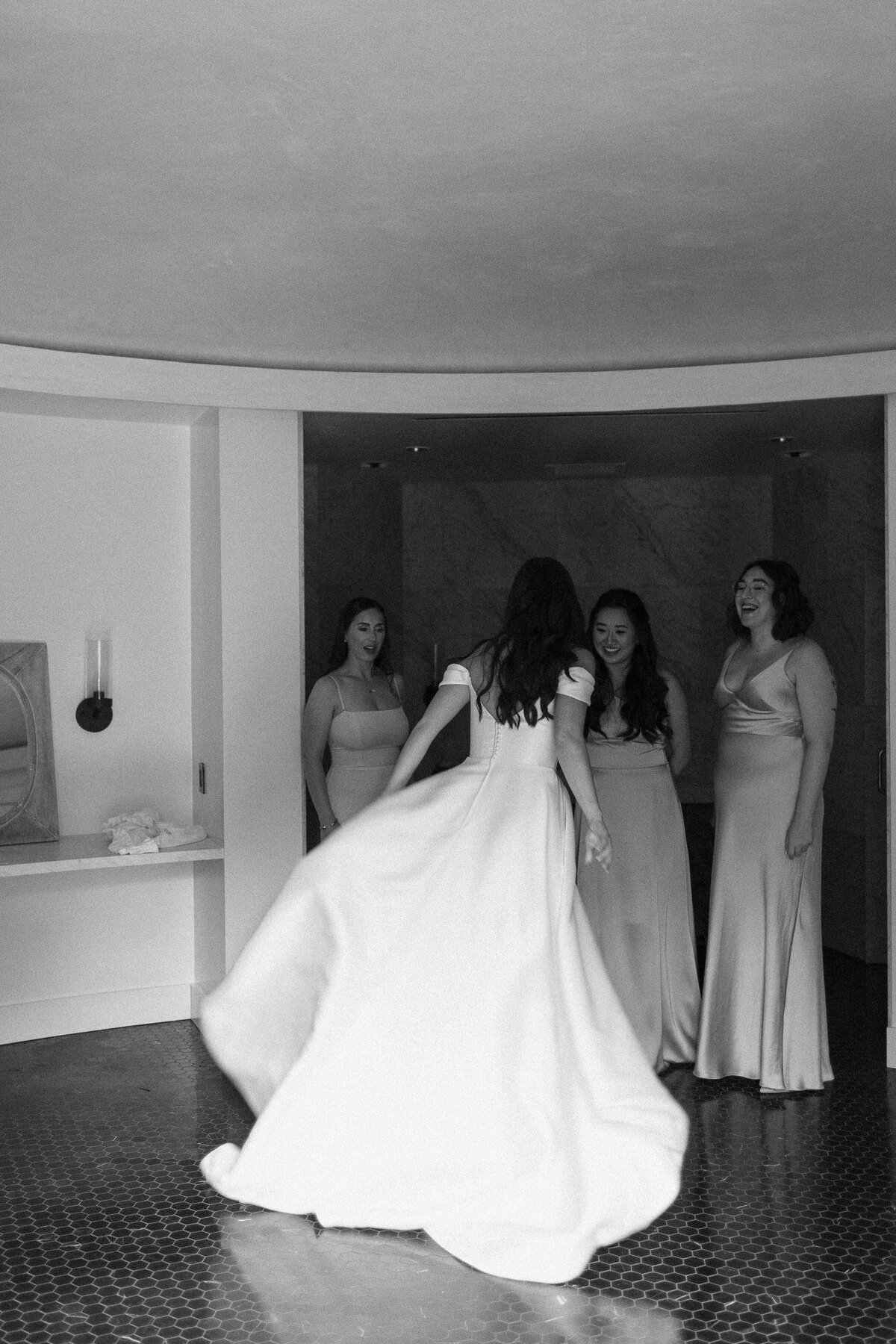 A joyous pre-wedding moment captured in black and white. The bride twirls in her stunning white gown inspiring smiles from her bridesmaids. A timeless and elegant shot of an intimate moment captures the full story of a wedding day.