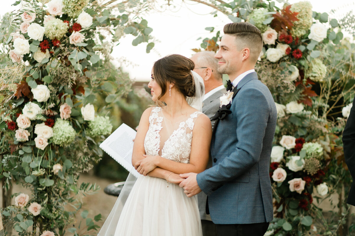 bride and groom standing under a full arch of flowers