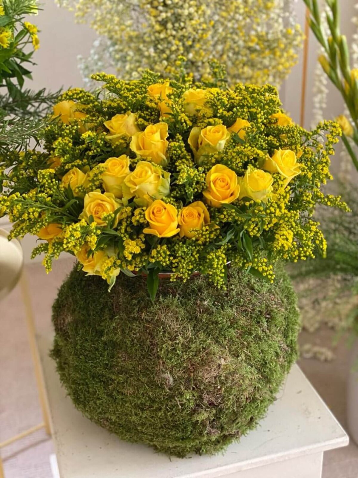 Bright yellow roses in a large moss covered vase