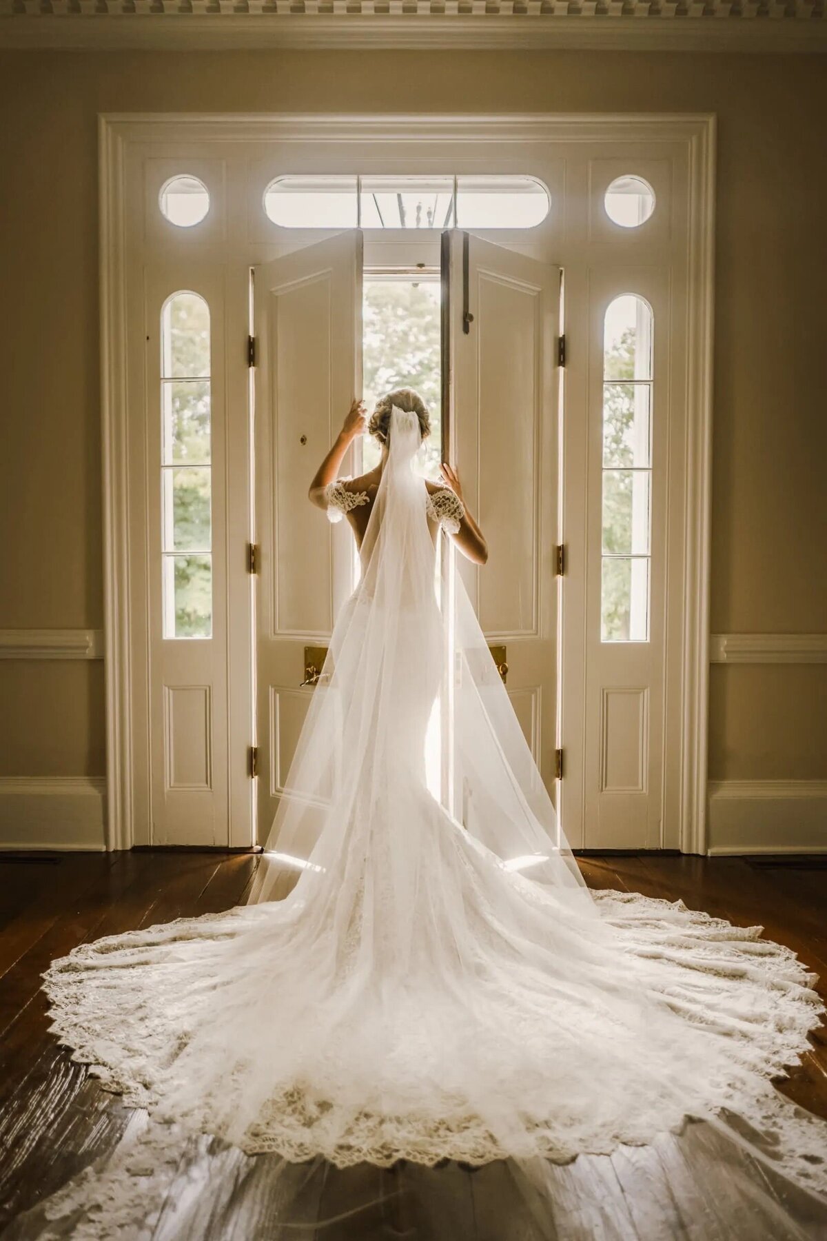 A bride illuminated by natural light from behind, her wedding dress and veil radiating