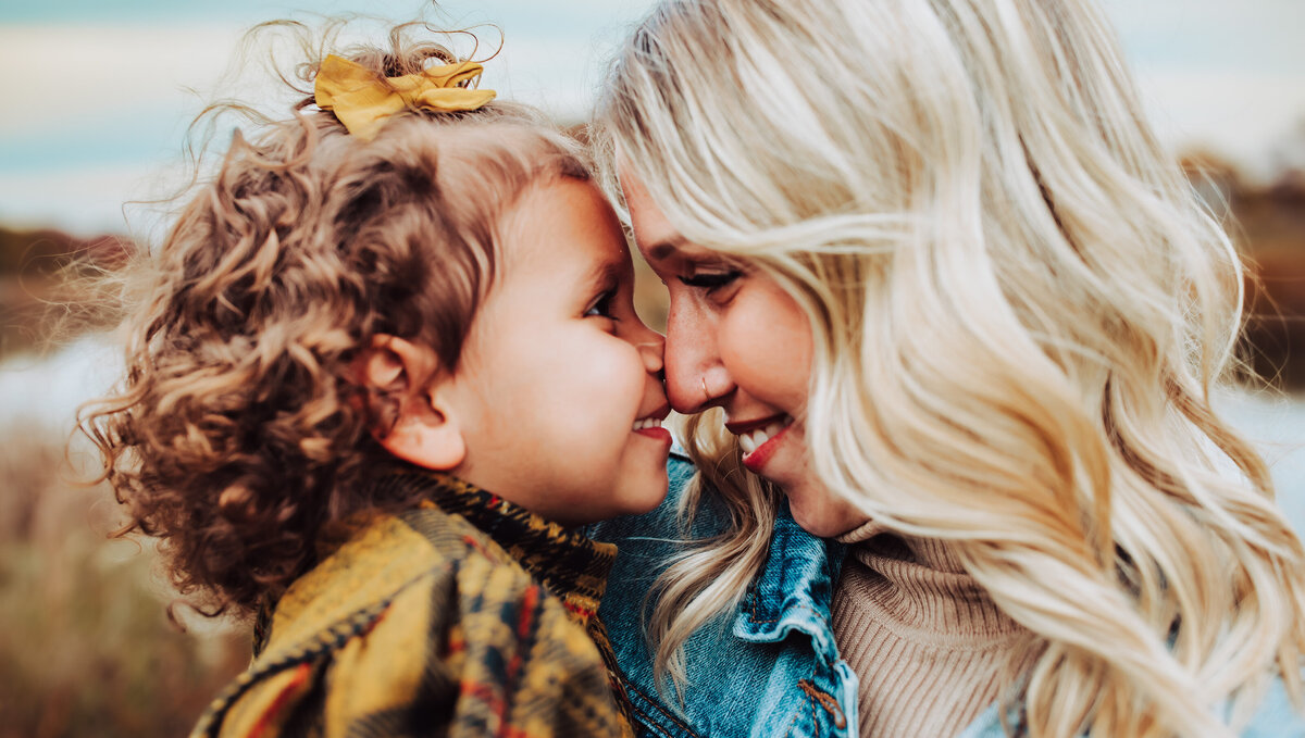 mom and daughter looking at each other, smiling at each other, curly hair, yellow bow, yellow dress, denim jacket,