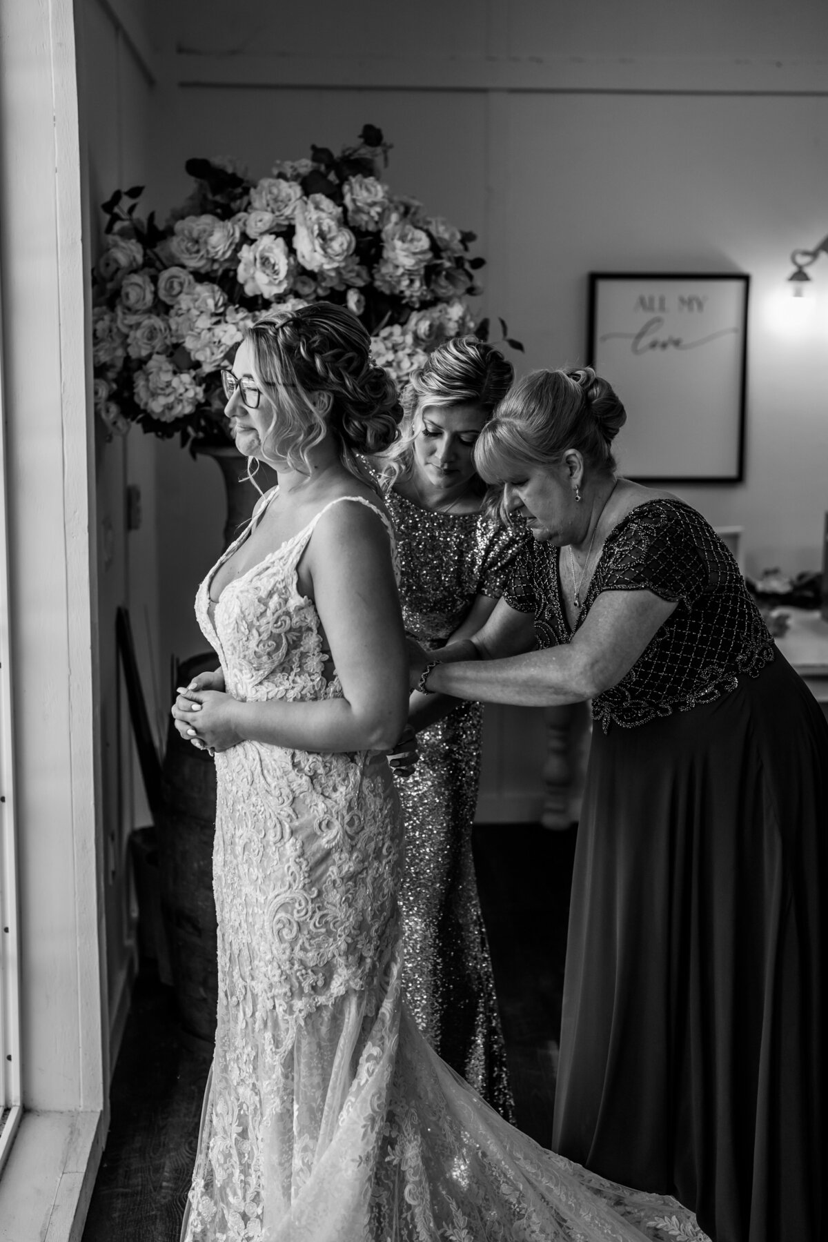 bride getting dressed with help from mom and friend staring out window