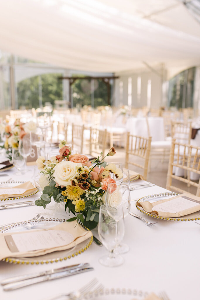 White tented wedding reception with white, yellow, pink, and burgundy Fall inspired florals designed by More Events Co, featured on the Brontë Bride Vendor Guide.