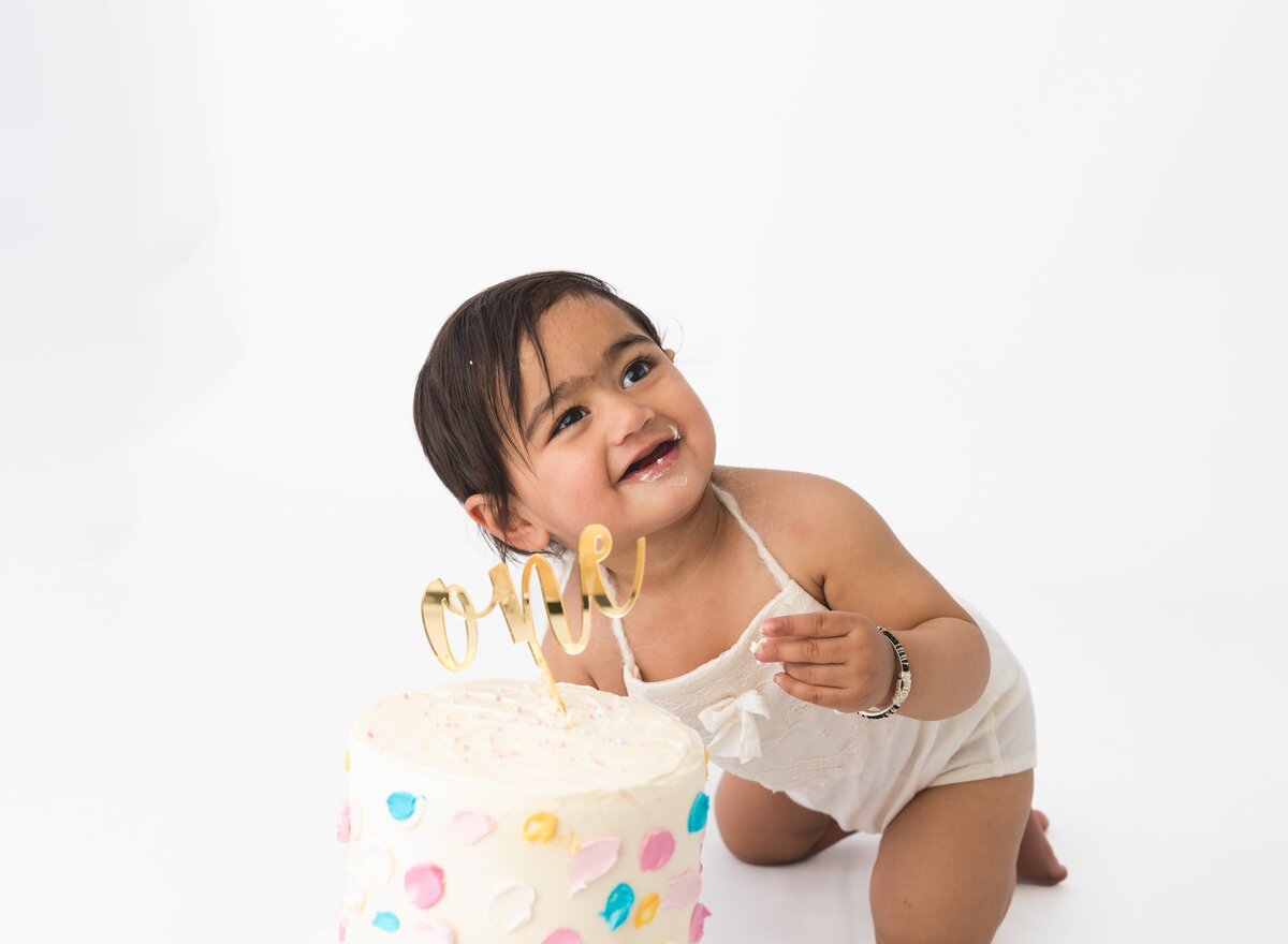 Baby wearing a big smile and sitting next to a cakesmash cake at a first birthday photoshoot by Hobart Photographer Lauren Vanier