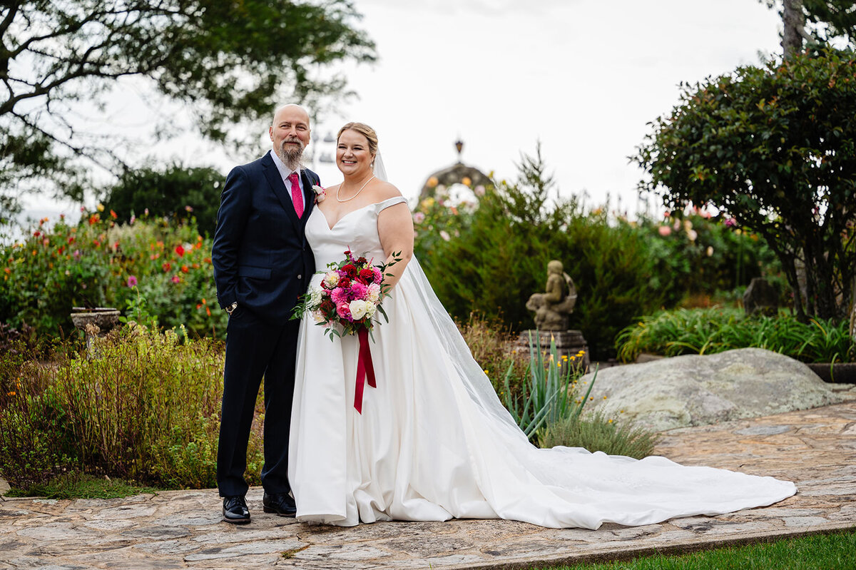 A bride and groom smiling and standing together on a stone path with a lush garden in the background