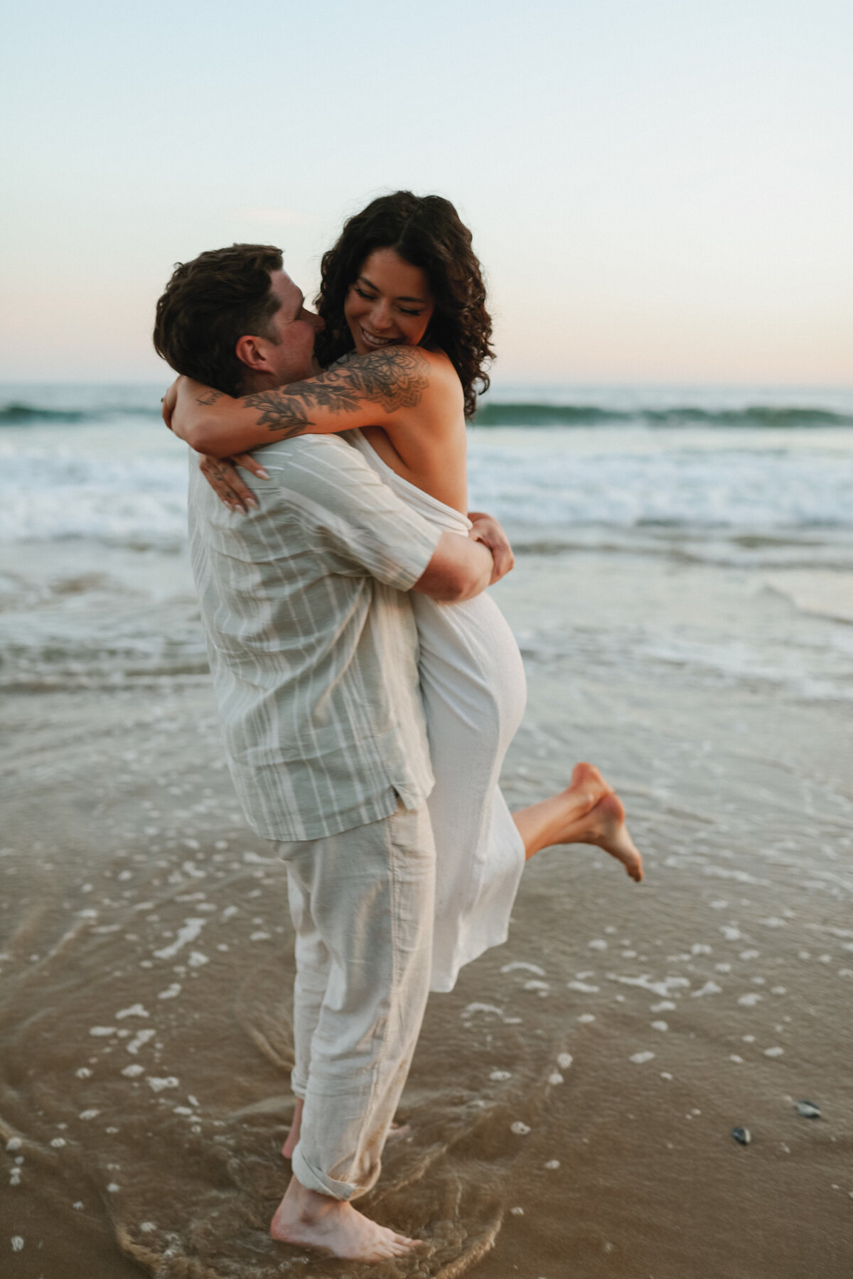 engagement photos at the beach , wearing white dress with waves in the back round