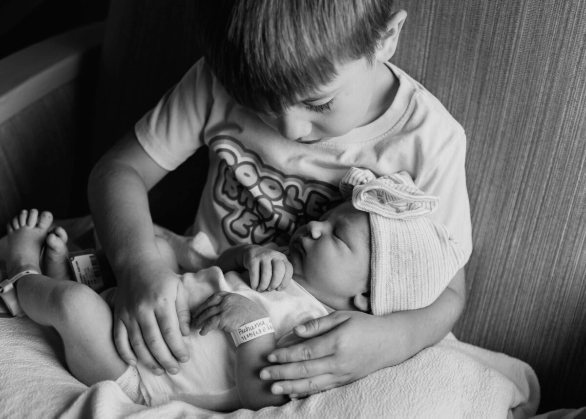A black and white photo of a boy holding a newborn baby captured by a Pittsburgh newborn photographer.