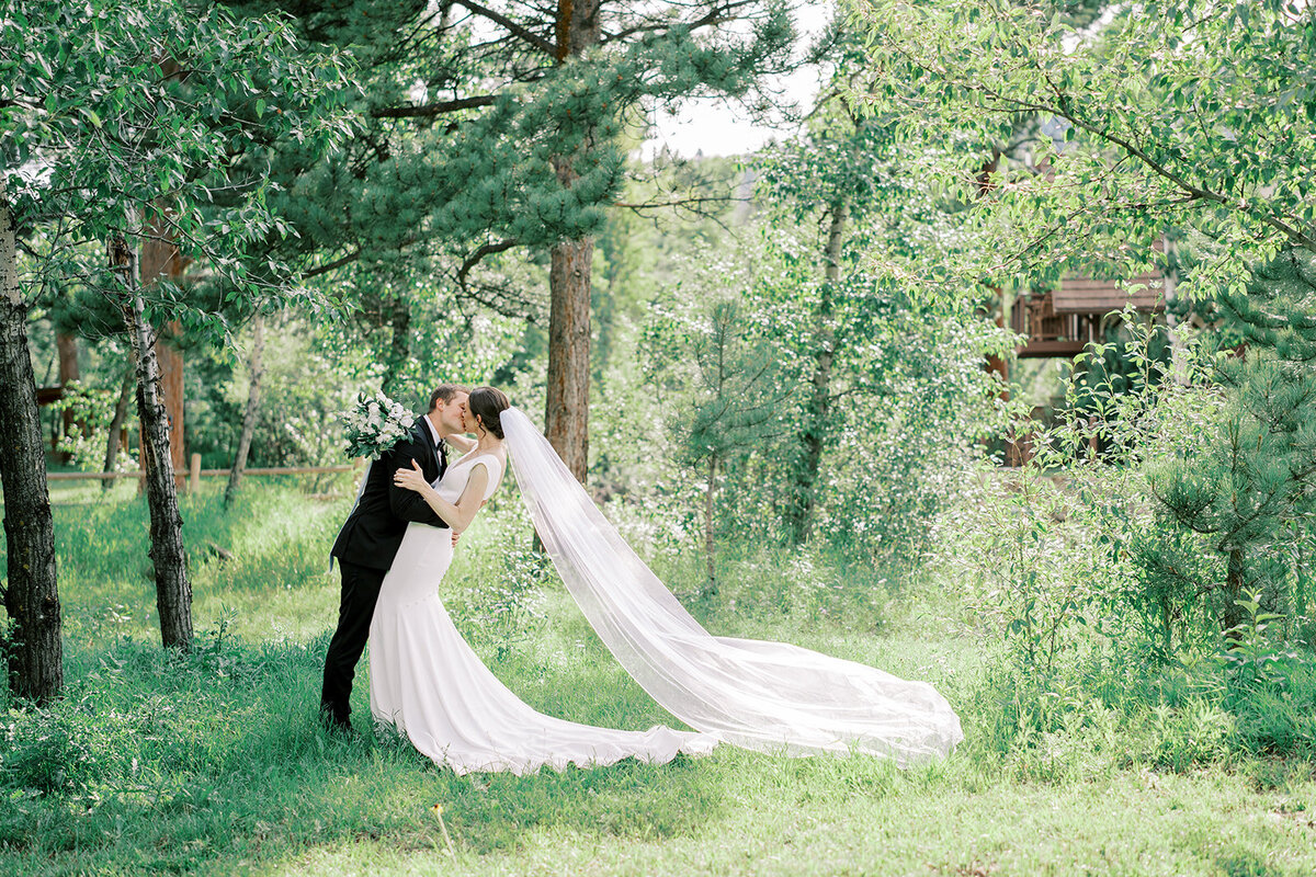 Bride and groom share a kiss in the trees at the Landing in Estes Park.