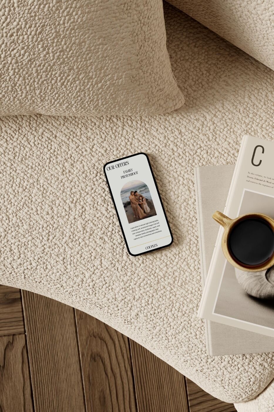 Smartphone resting on a cream textured sofa beside an open magazine and a coffee cup, screen showing a photographer’s “Our Offers” page with a family photoshoot session and descriptive text.