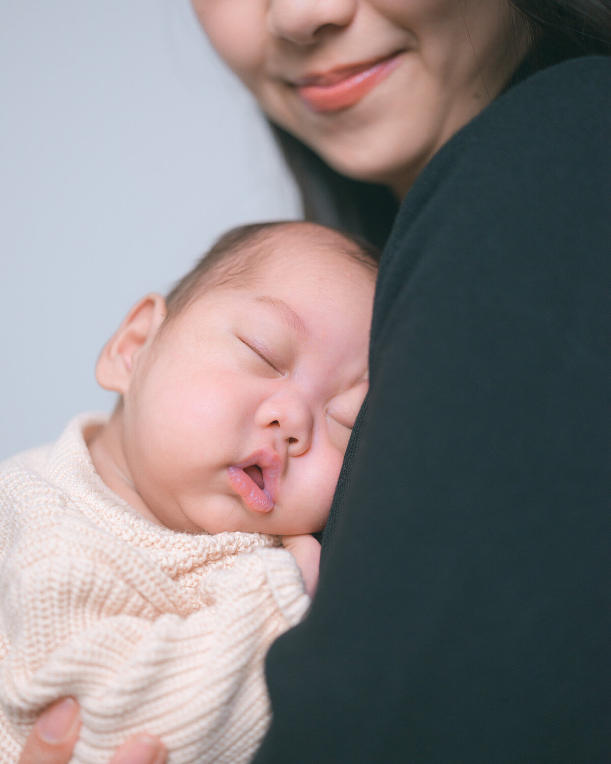 Newborn baby sleeping in a mother’s arms, photographed by a top Palo Alto newborn photographer. Natural in-home baby photography capturing authentic, peaceful