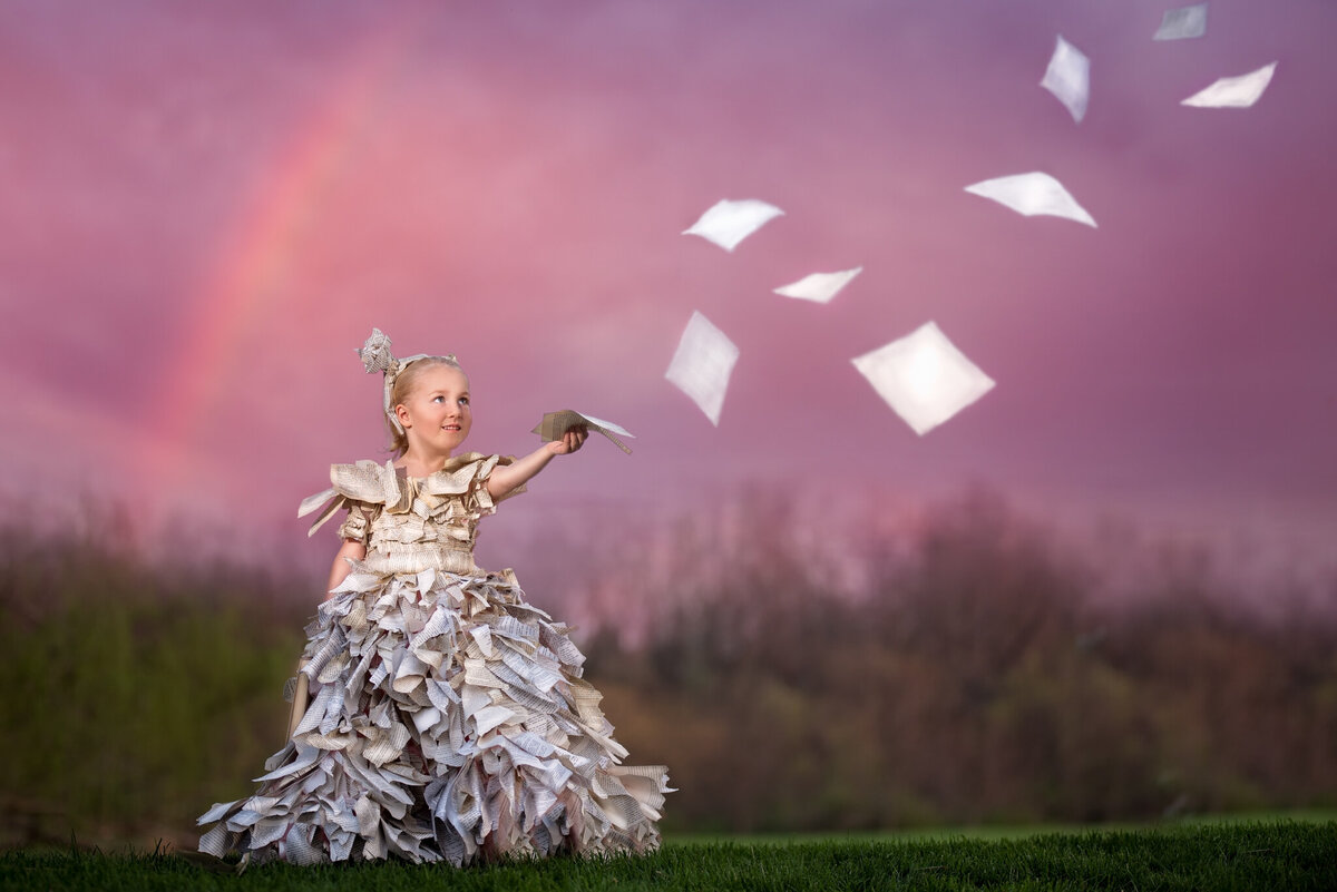 Whimsical portrait of a young girl surrounded by floating papers in a dreamlike outdoor setting, captured in Overland Park, Kansas. Ideal for families looking for imaginative and artistic child photography in the Kansas City area.