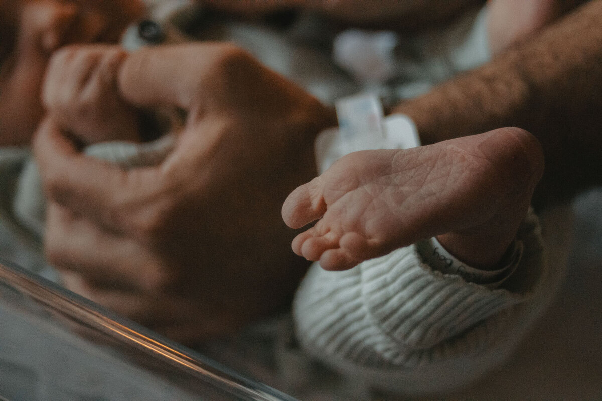 Close-up of a newborn’s feet held tenderly by their father