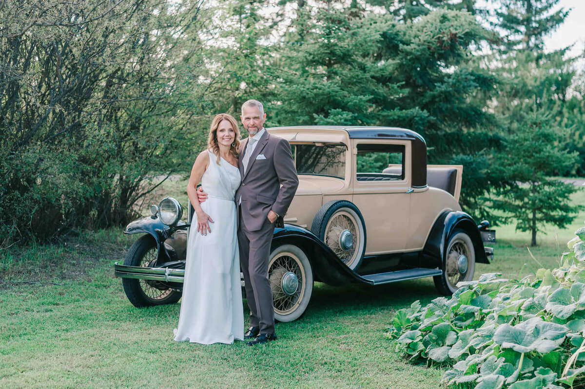 Bride and groom standing in front of a black and tan car.