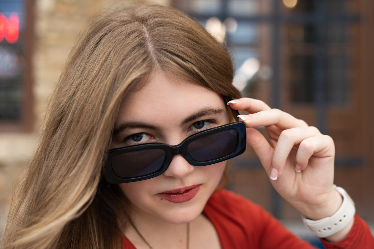 A senior girl looking over her sunglasses in downtown Lawrence, KS