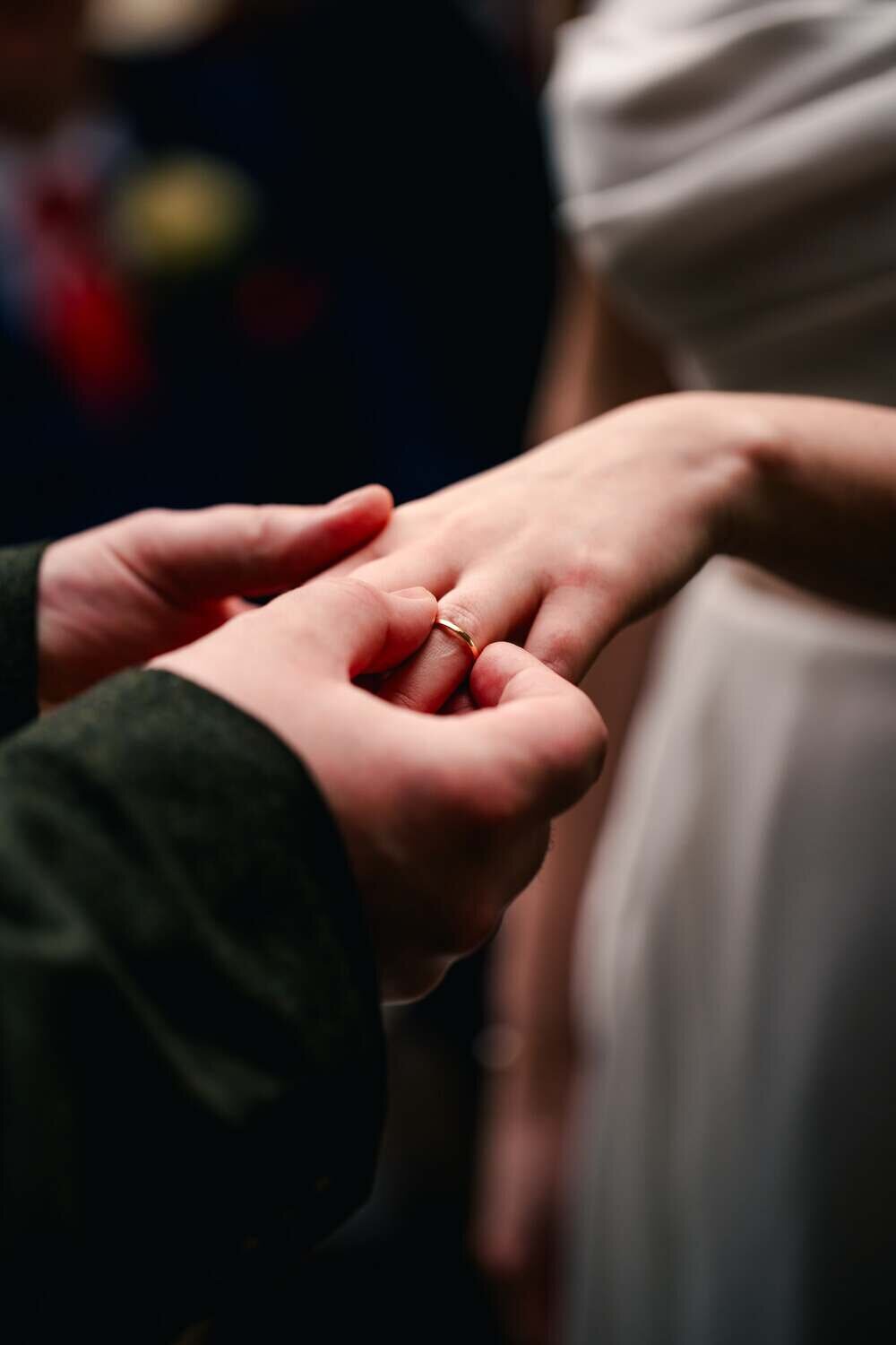Grrom places wedding ring on brides finger