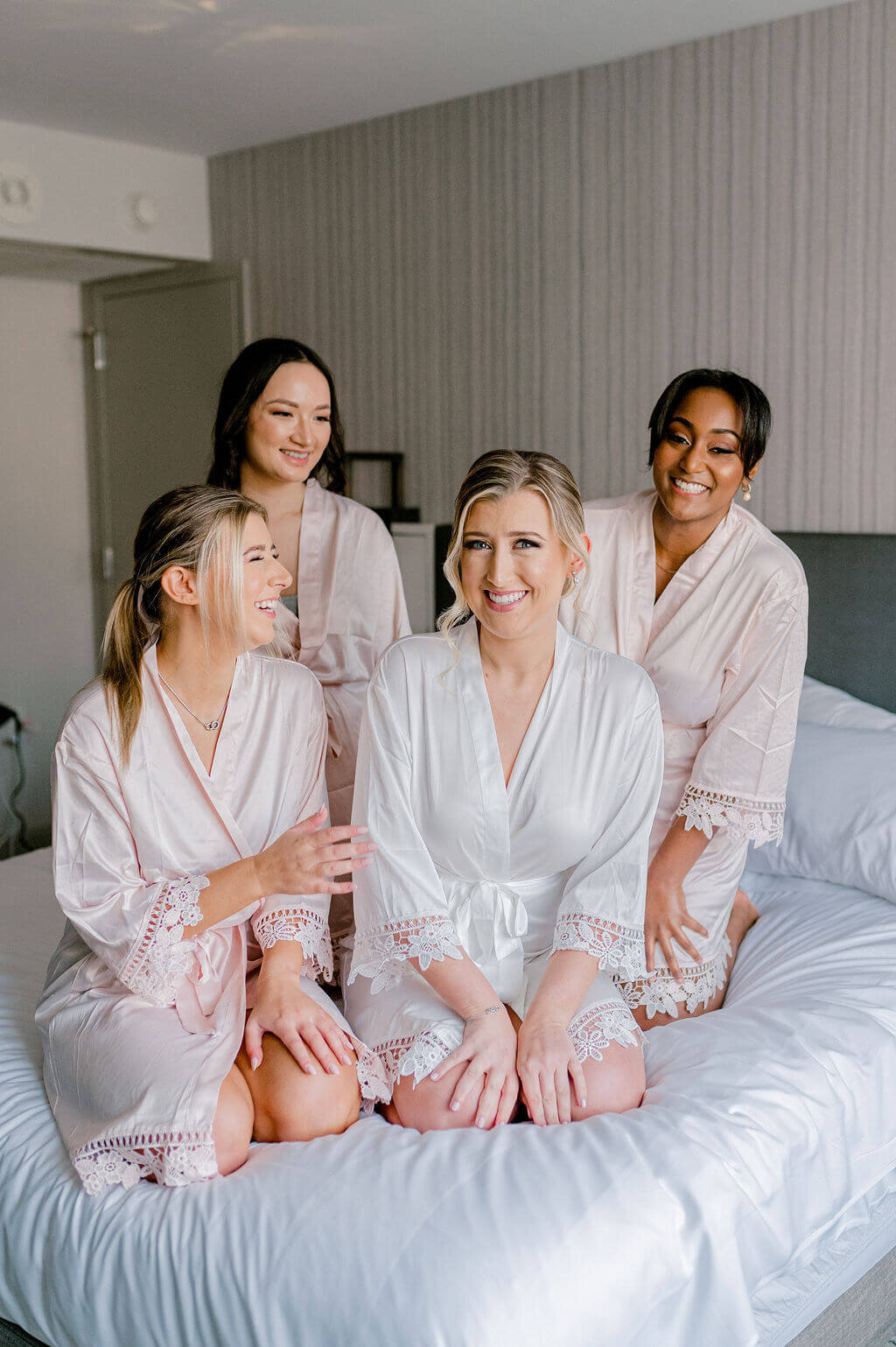 Bridal party in Georgetown hotel in matching robes smiling at one another while sitting on bed.