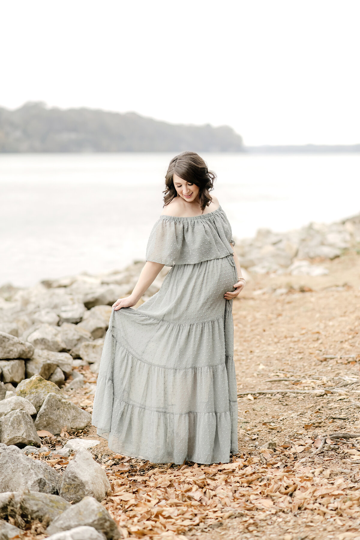 Pregnant woman in teal dress by river and rocks