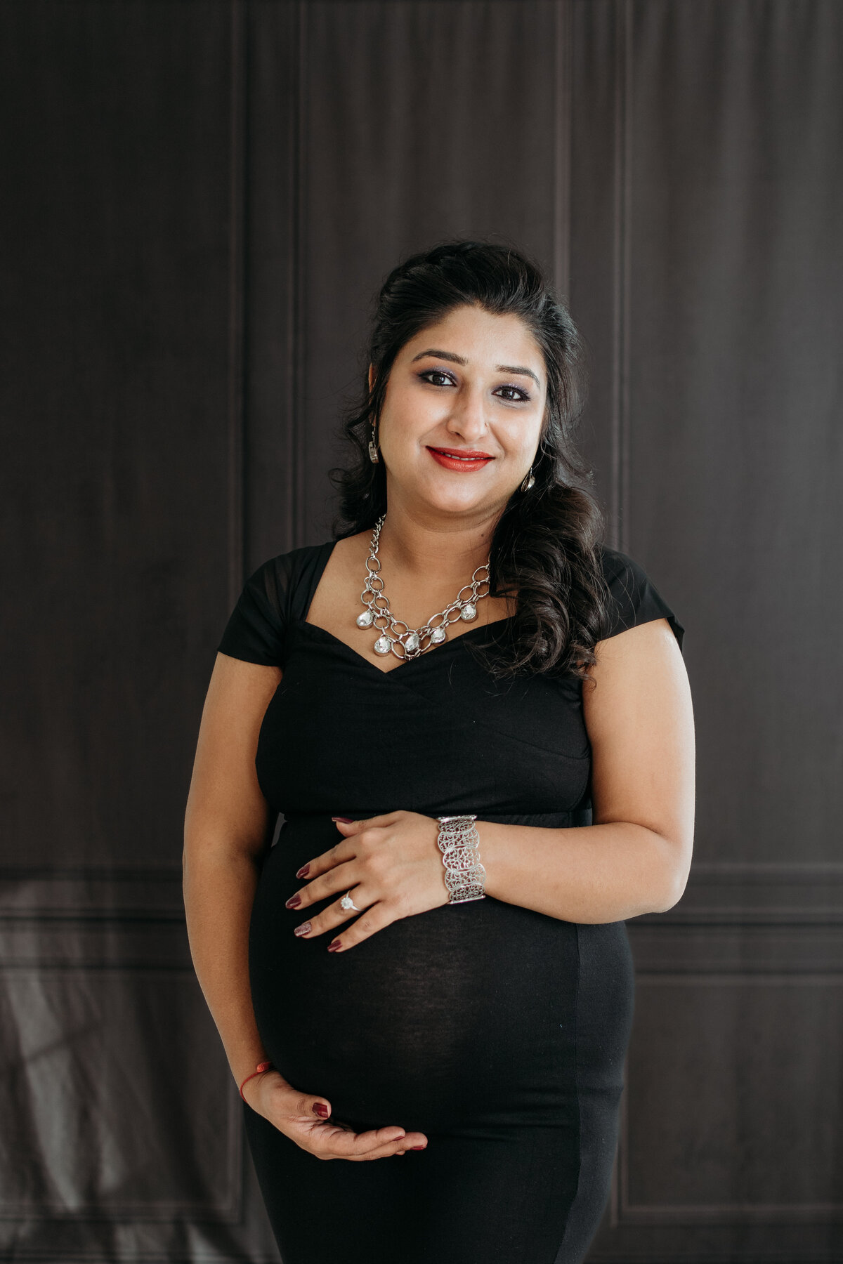 Pregnant mom in a black dress glowing of beauty and embracing her jewels during a studio maternity photoshoot in Winfield, IL