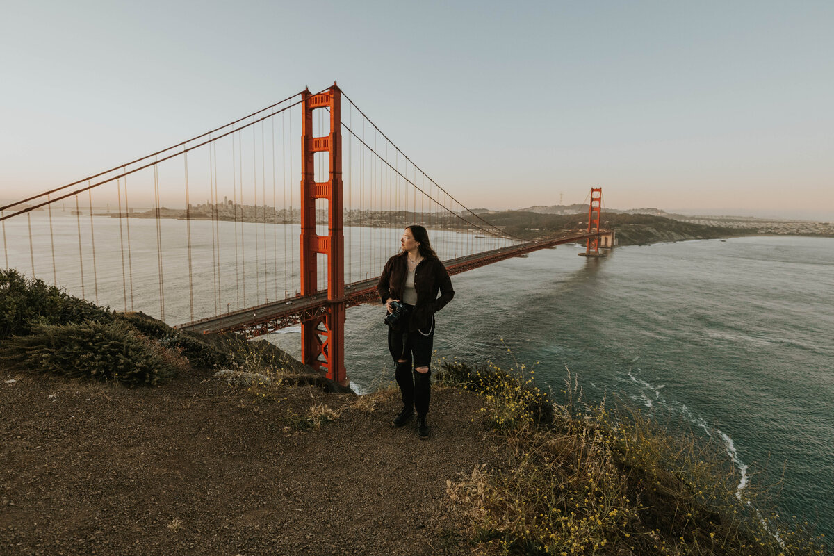 woman standing on cliff next to ocean and golden gate bridge
