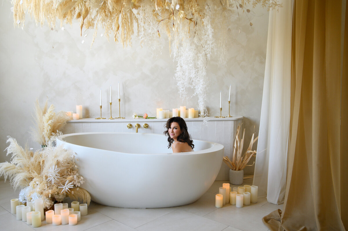 woman with brown hair sitting in a tub with pampas and curtains for her boudoir photography session.