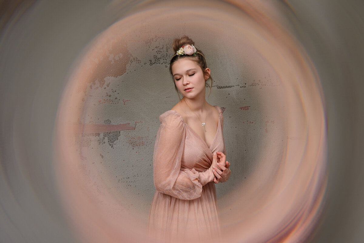Soft portrait of a woman in a pink dress, surrounded by a blurred circular effect, with a floral hairpiece