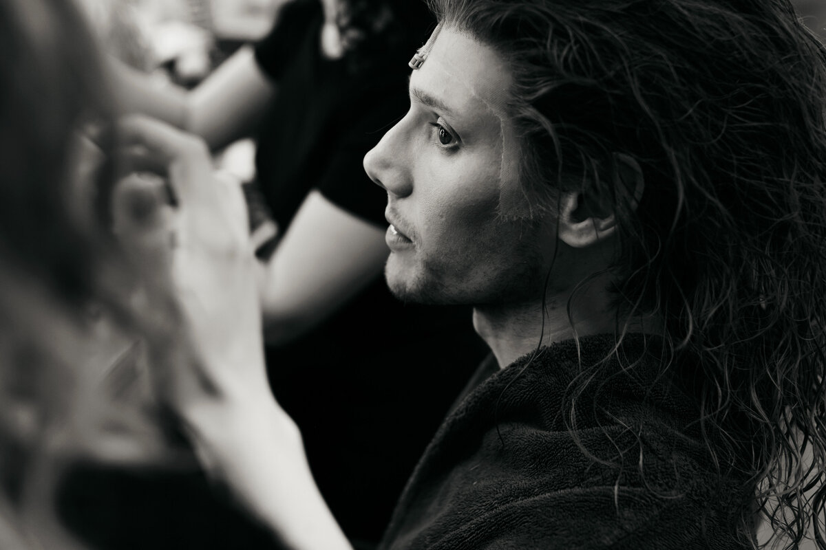 Backstage portret van visagisten die werken aan langharige pruik op hoofd van acteur.