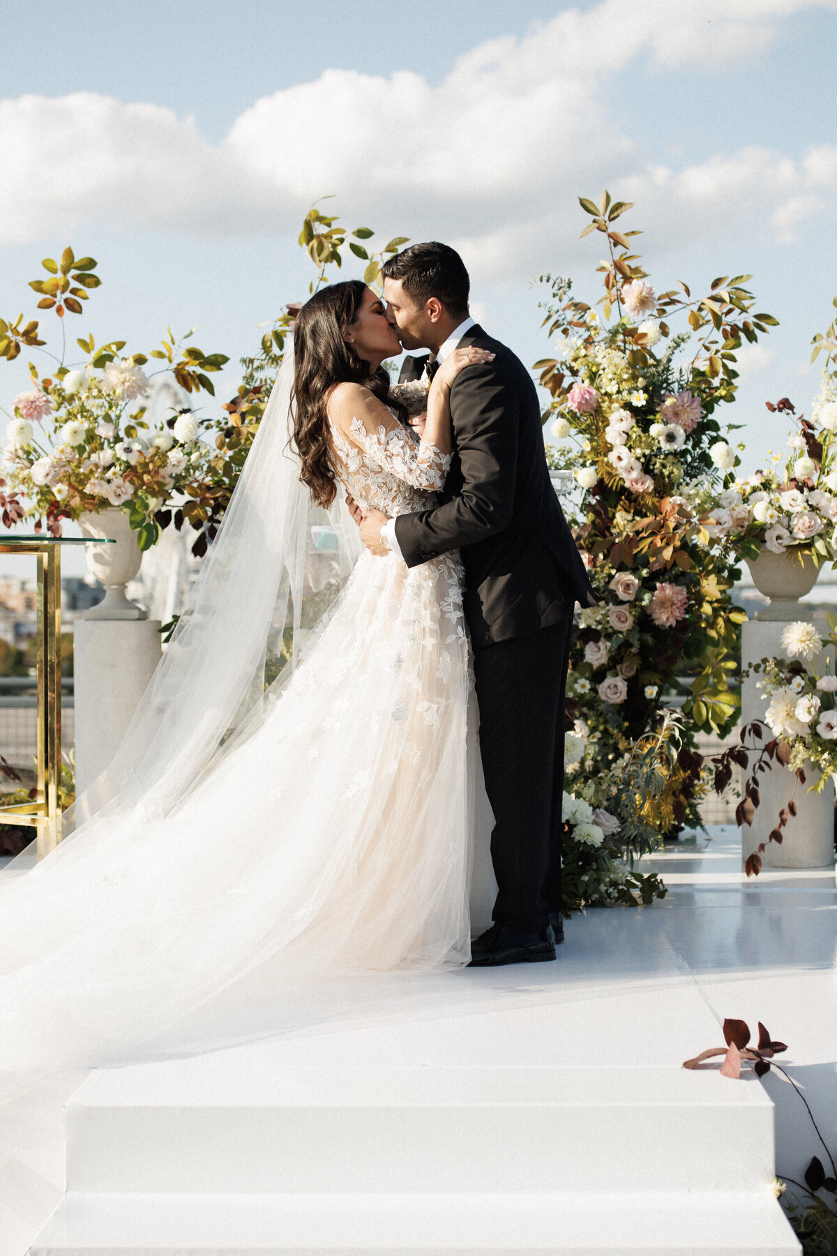 A bride and groom embrace on the roof of the Science Centre surrounded by lush flowers.