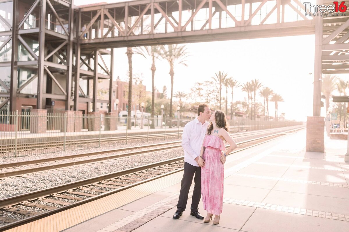 Engaged couple share a kiss next to the train tracks