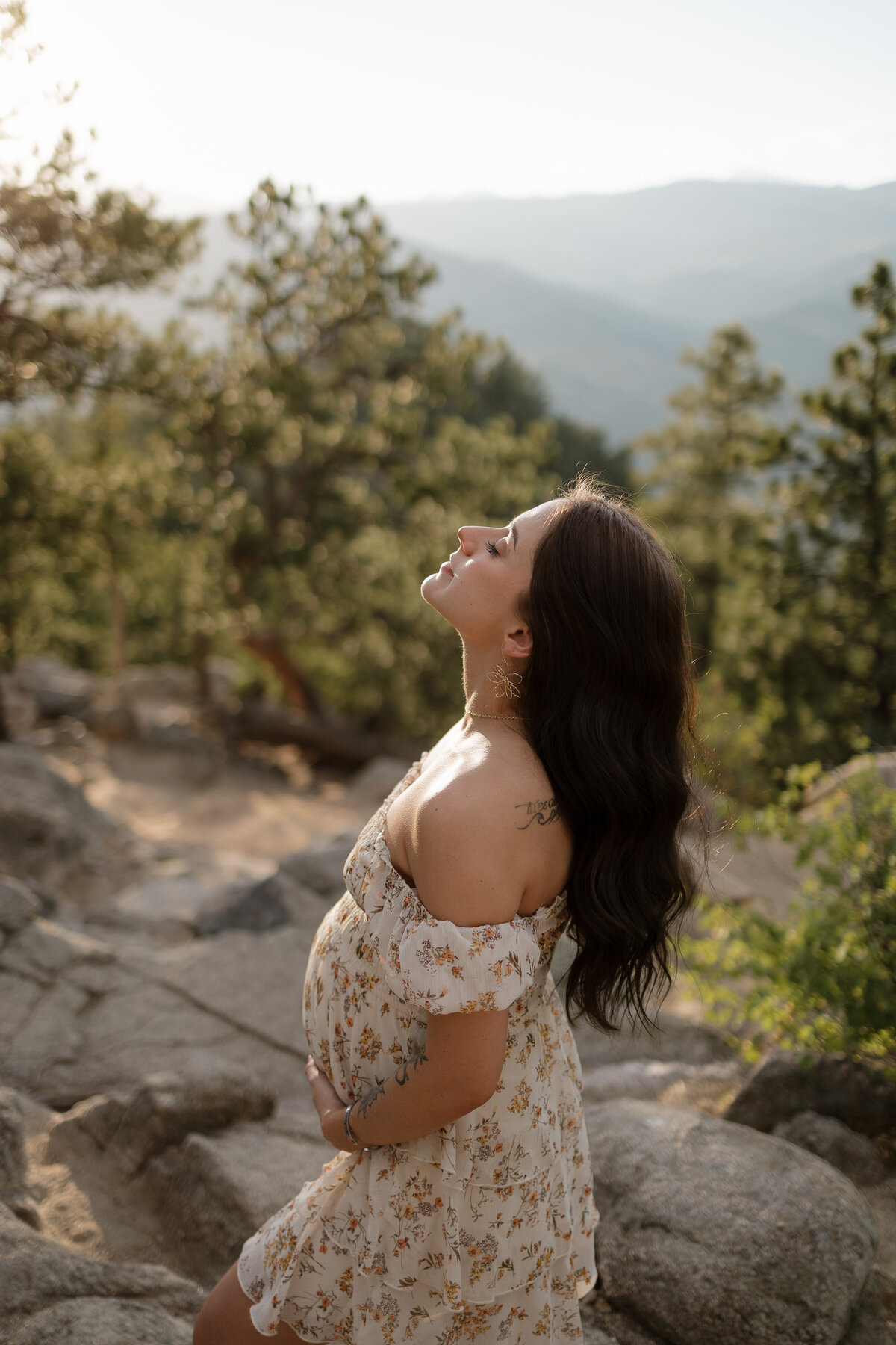 Expectant mom holding belly while head is tilted up towards the sky with her eyes closed during lifestyle maternity session in boulder colorado with alexis adkins photo