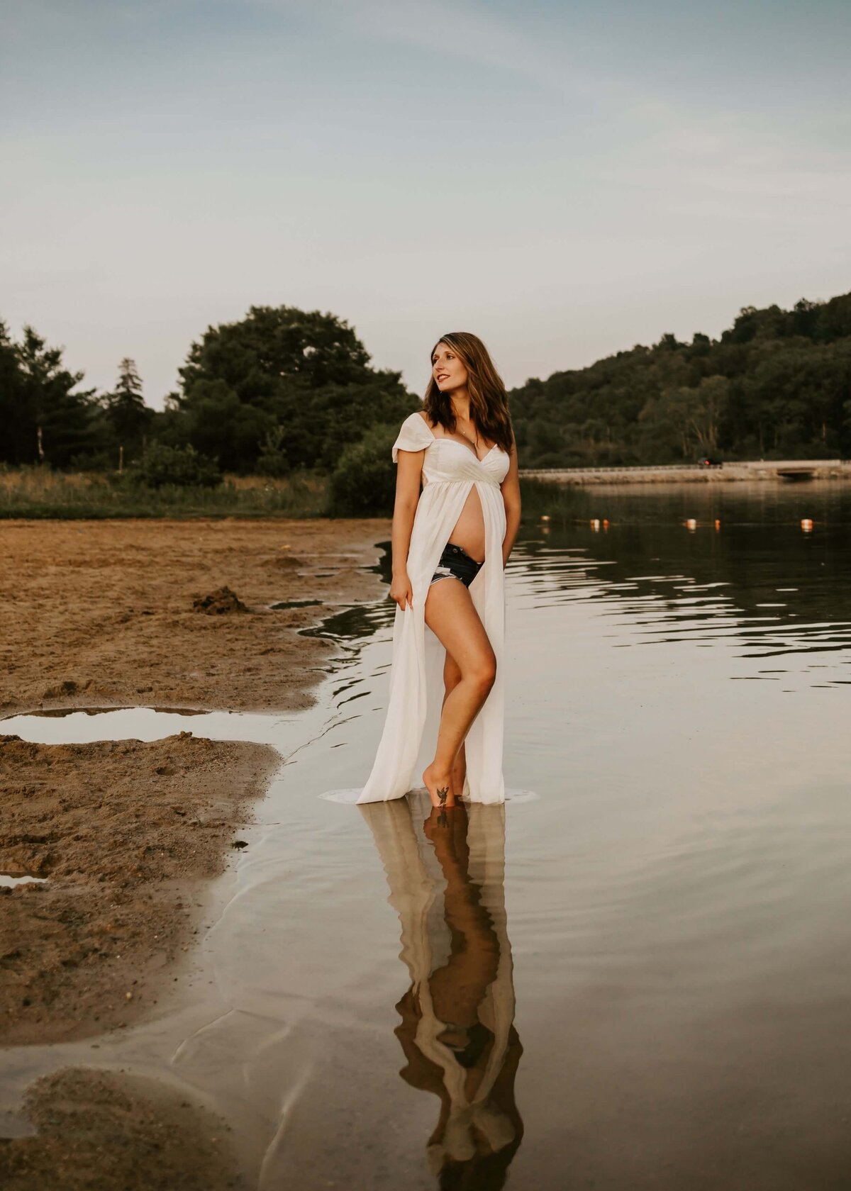 A pregnant woman standing in the water at sunset, captured by a Pittsburgh maternity photographer.