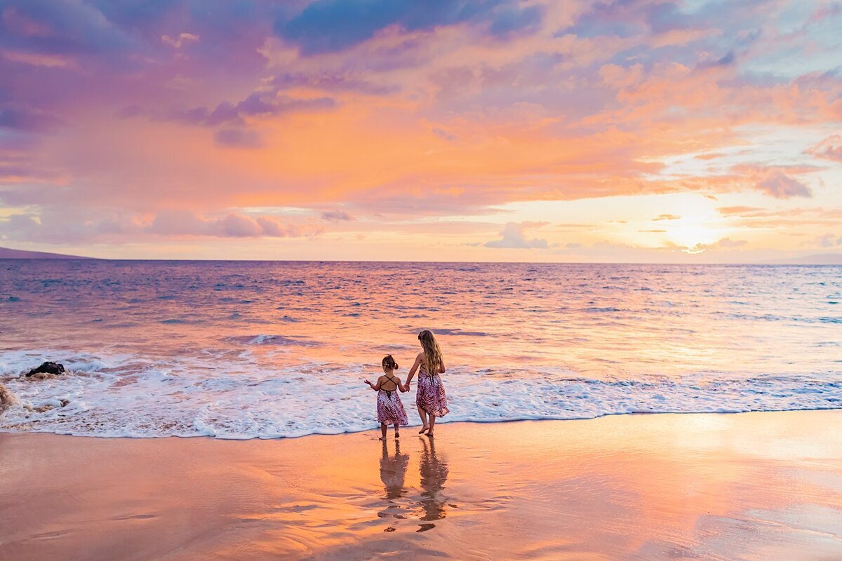 Two girls run toward the ocean holding hands as a family during a sunset portrait session in Wailea
