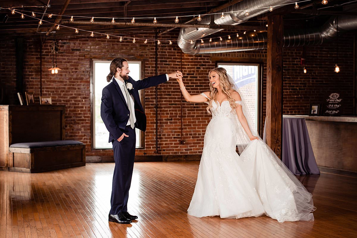 Bride and groom dancing together in the open bar area of Cannery Ballroom with vintage bricks and bistro lights