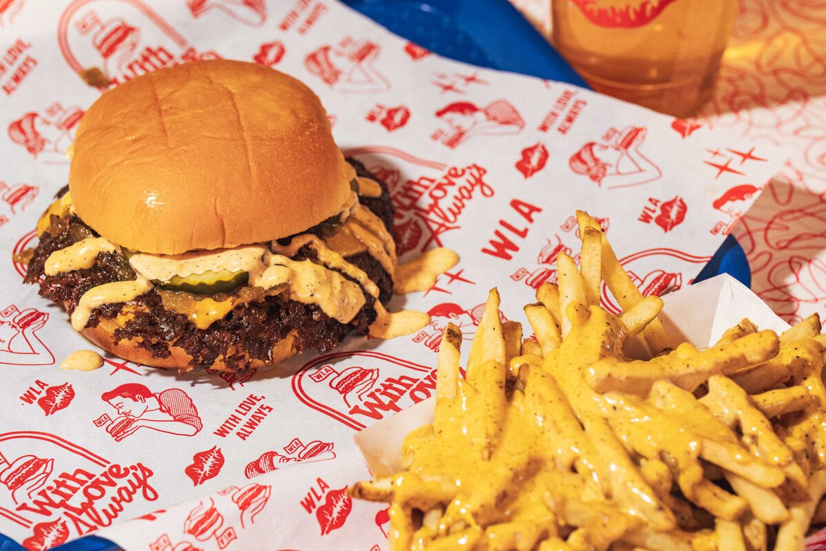 Close-up of a classic smashburger with pickles, grilled onions, and special sauce next to beef tallow fries with cheddar sauce at With Love, Always in Las Vegas