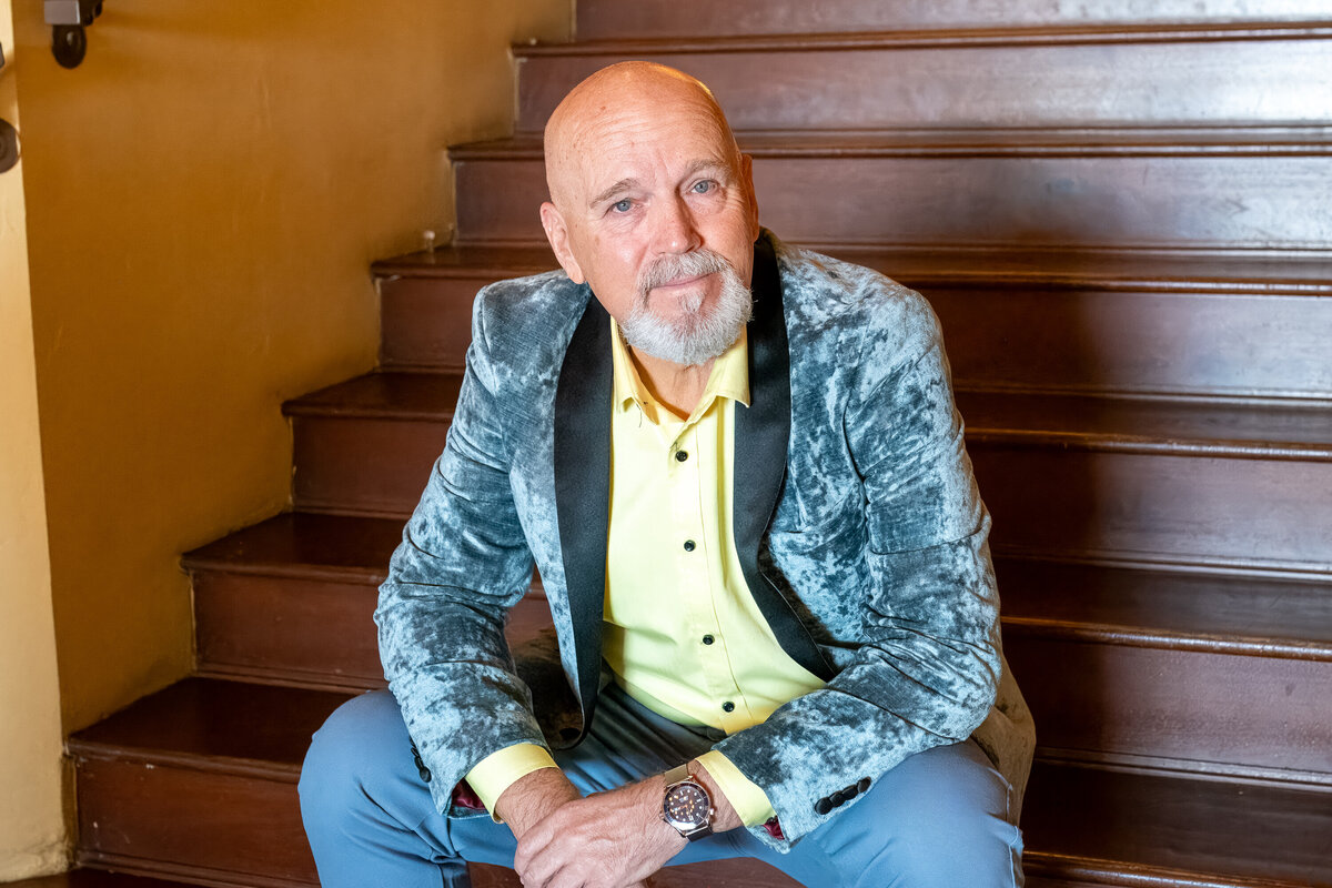 Man sitting on wooden stairs in a stylish blazer and yellow shirt, looking confidently at the camera, photographed by Vyrl Photo, showcasing Tucson brand photography.