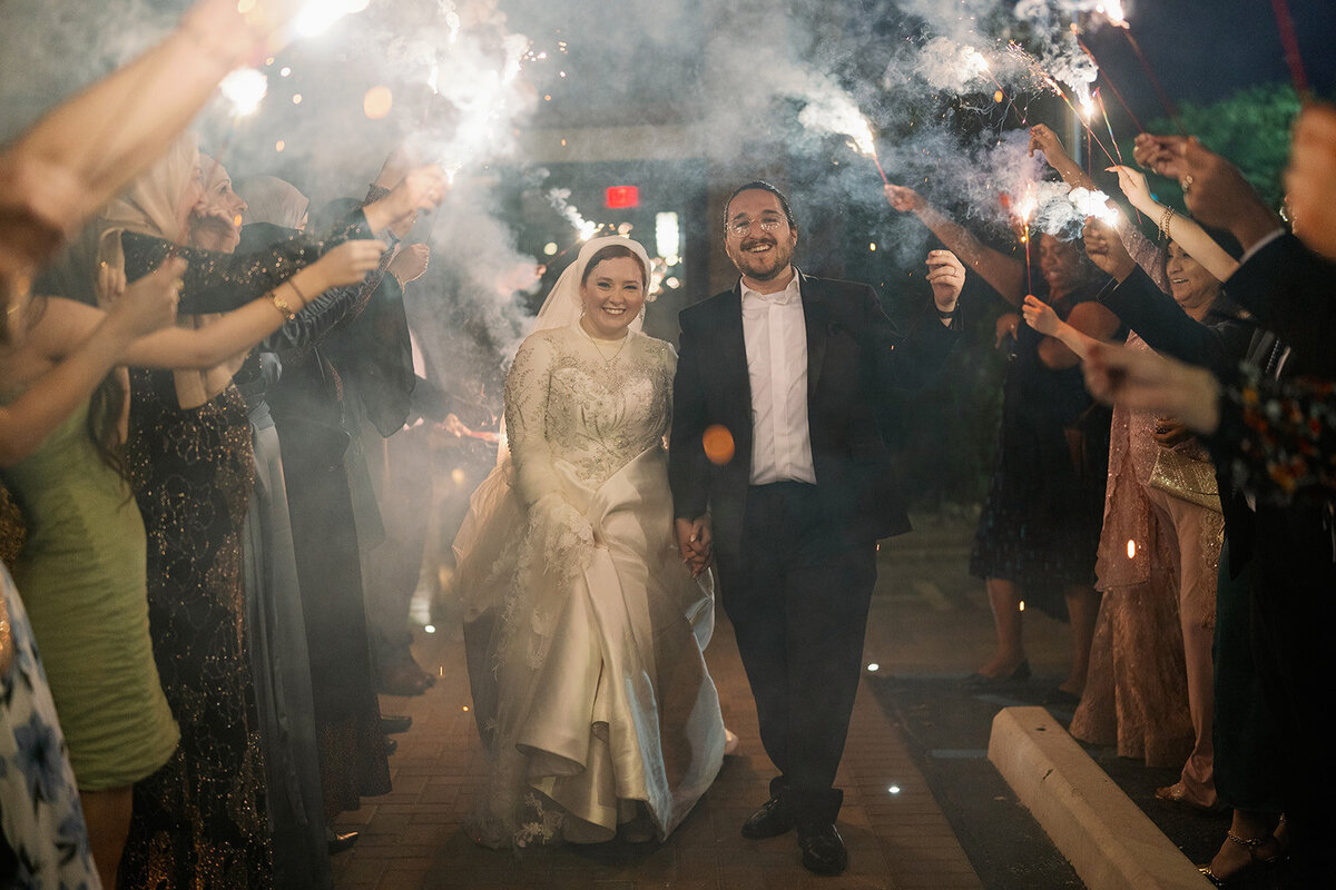 Bride and groom walking through a sparkler exit surrounded by guests during their Dearborn Michigan wedding celebration.
