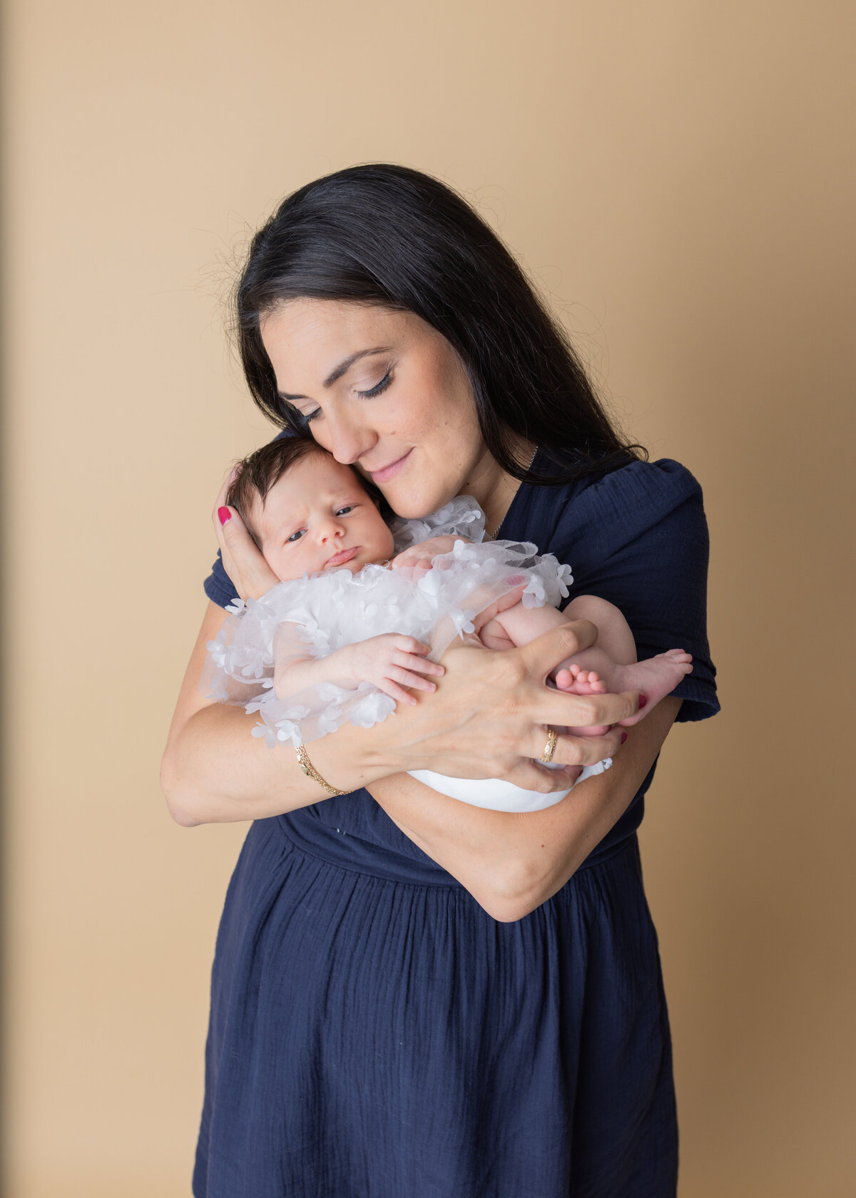 Mother lovingly cuddling her newborn baby girl in a white floral outfit during a lifestyle newborn session in Waldwick New Jersey