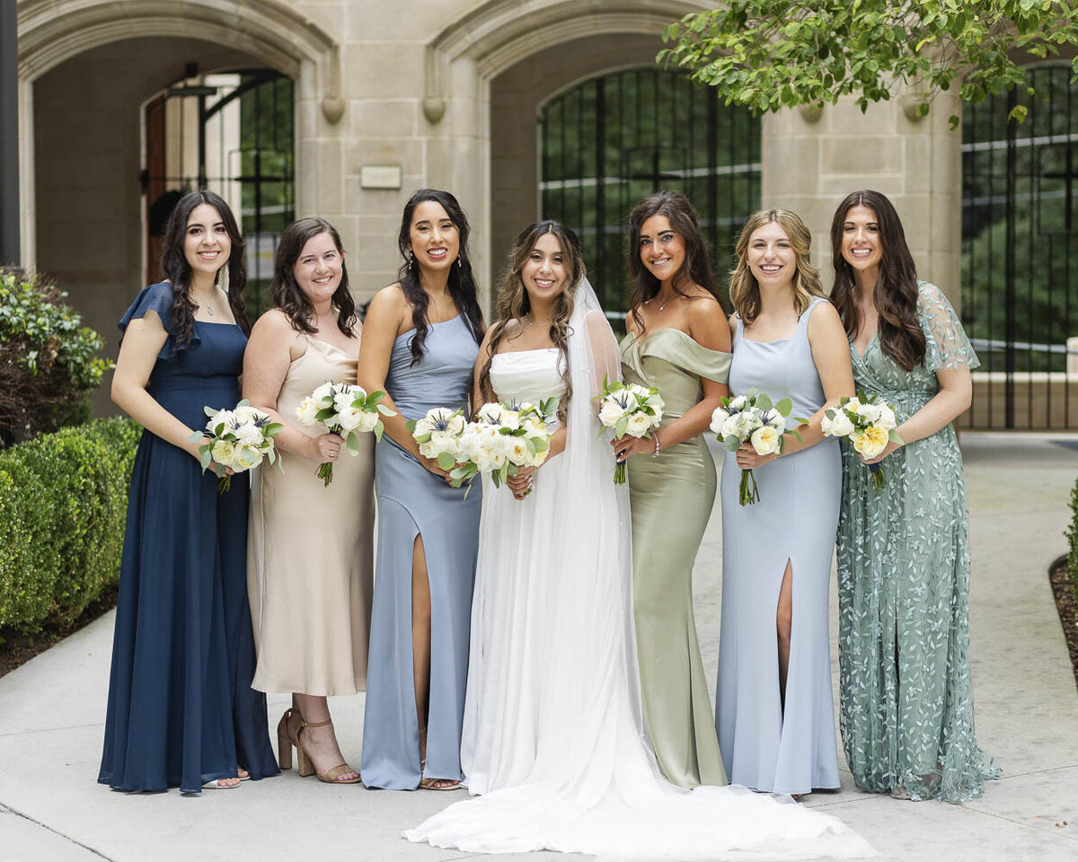bride posing with bridesmaids in dresses that are various shades of blue