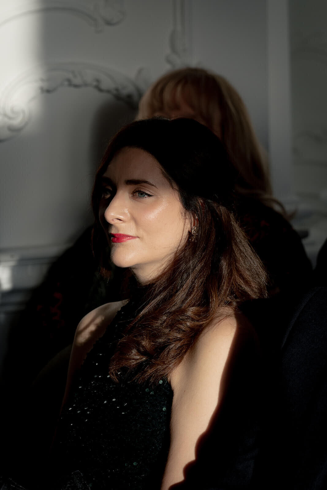The sun shines on the face of a seated wedding guest with red lips